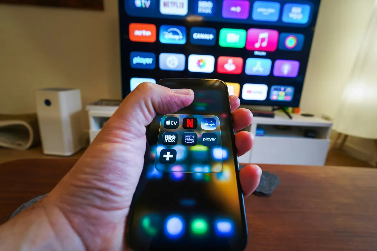 A hand holding a remote control in front of a television