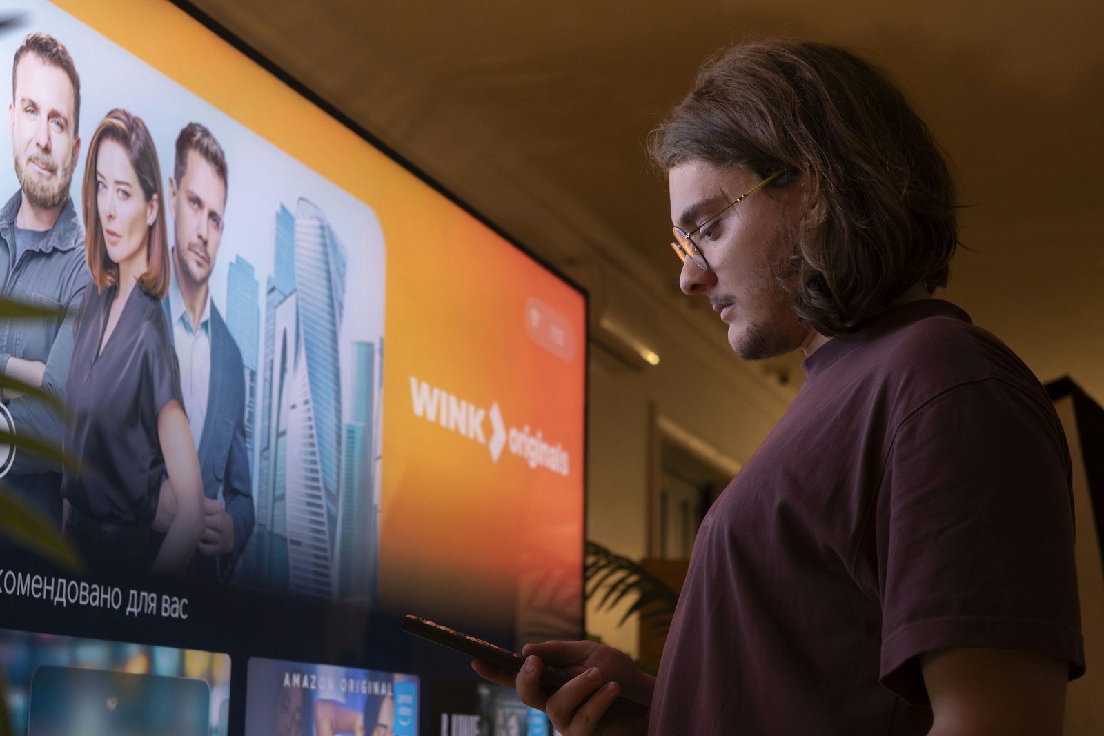 A person holding a remote in front of a bright television in a modern living room